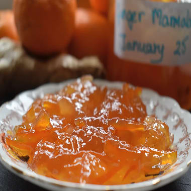 Ginger Marmalade on a small plate with Seville oranges, ginger and a jar of marmalade in the background.